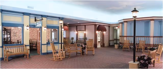 Indoor common area resembling a small covered street with benches, rocking chairs, lampposts, and storefront-style facades.