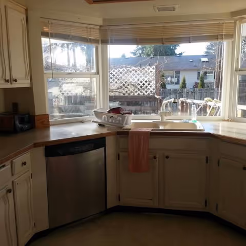 Kitchen with sink under bay windows, dish rack, and white cabinets.