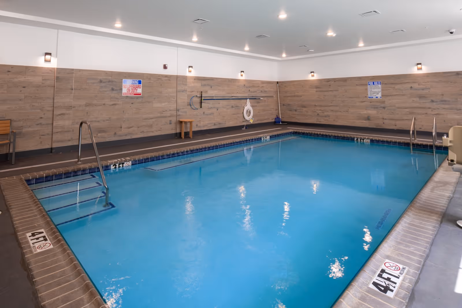 Indoor rectangular swimming pool in a wood-paneled room with ladders, a life ring and depth markings.