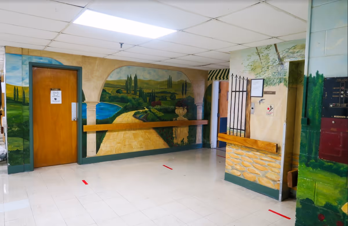 Interior hallway with a large painted mural of a garden pathway, handrails, doors, and a tiled floor.