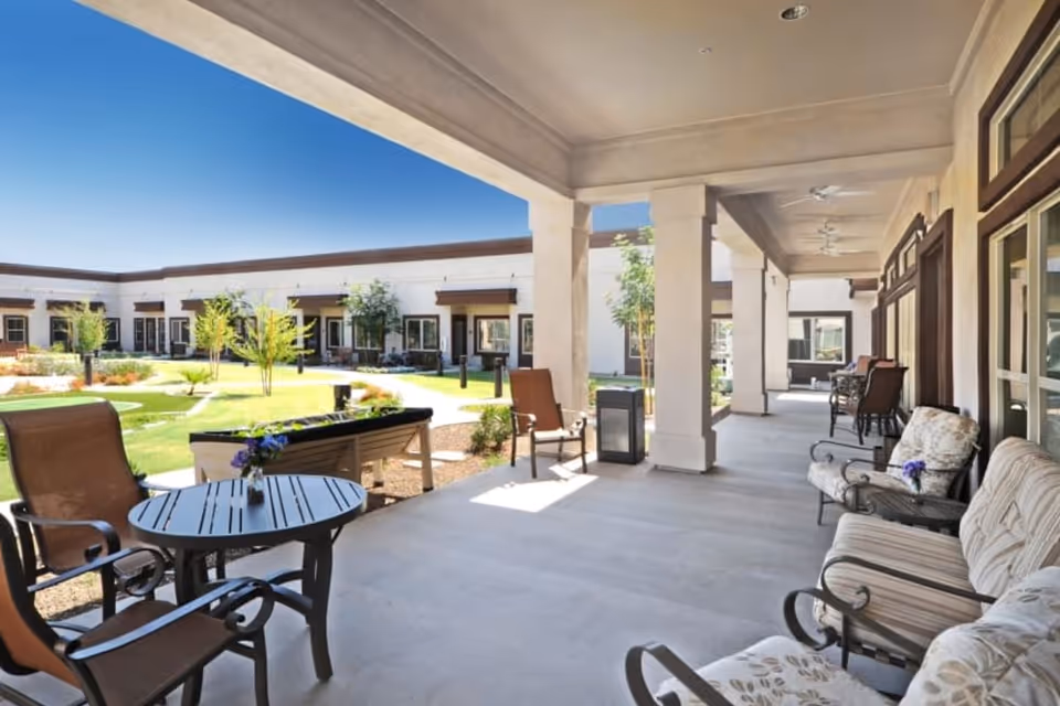 Covered outdoor patio with chairs, tables, and cushioned seating overlooking a landscaped central courtyard.