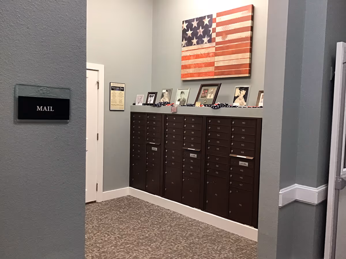 Hallway mail area with rows of brown resident mailboxes beneath an American flag wall art and a 'MAIL' sign.