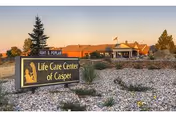 Exterior view of Life Care Center of Casper building during sunset with a landscaped area featuring rocks and plants in the foreground and a sign displaying the facility's name and address.