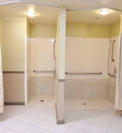 Two accessible walk-in showers with grab bars in a tiled senior bathroom.