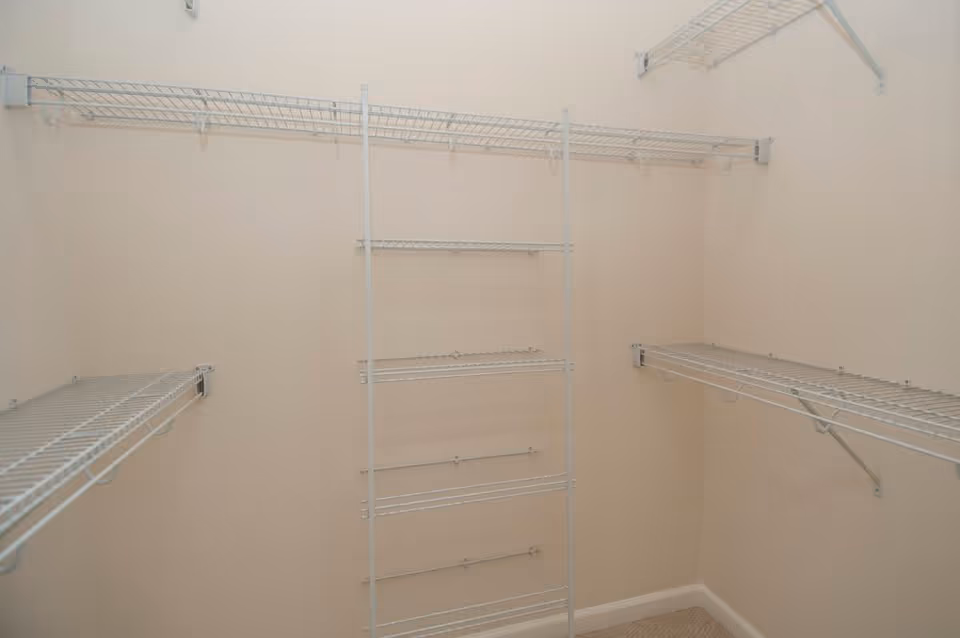 Empty walk-in closet with beige walls and white wire shelving on three sides.