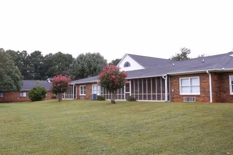 Brick senior living facility with a green lawn and screened porch fronting the building