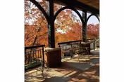 Covered outdoor patio with metal chairs and tables overlooking trees with autumn foliage.