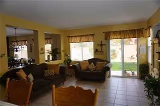 Sunlit living room with couches, large windows, and a doorway to a green outdoor area.