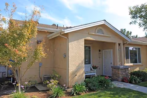 Beige stucco senior apartment building front entrance with a porch and garden.