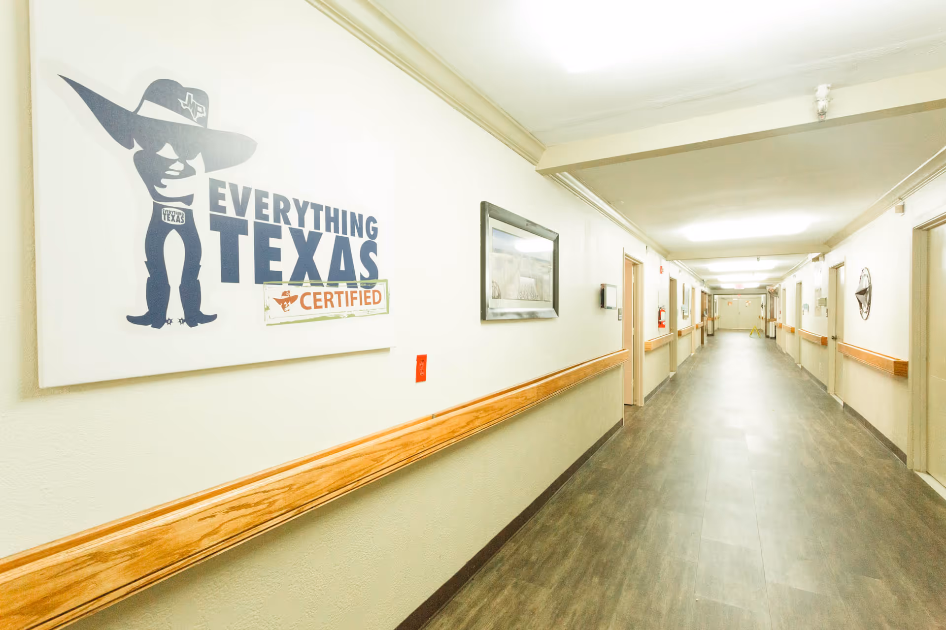 Bright long interior hallway with wood handrails, doors along both sides, and a large "Everything Texas Certified" wall sign.