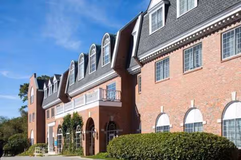 Brick senior living facility front exterior with arched windows and manicured shrubs.