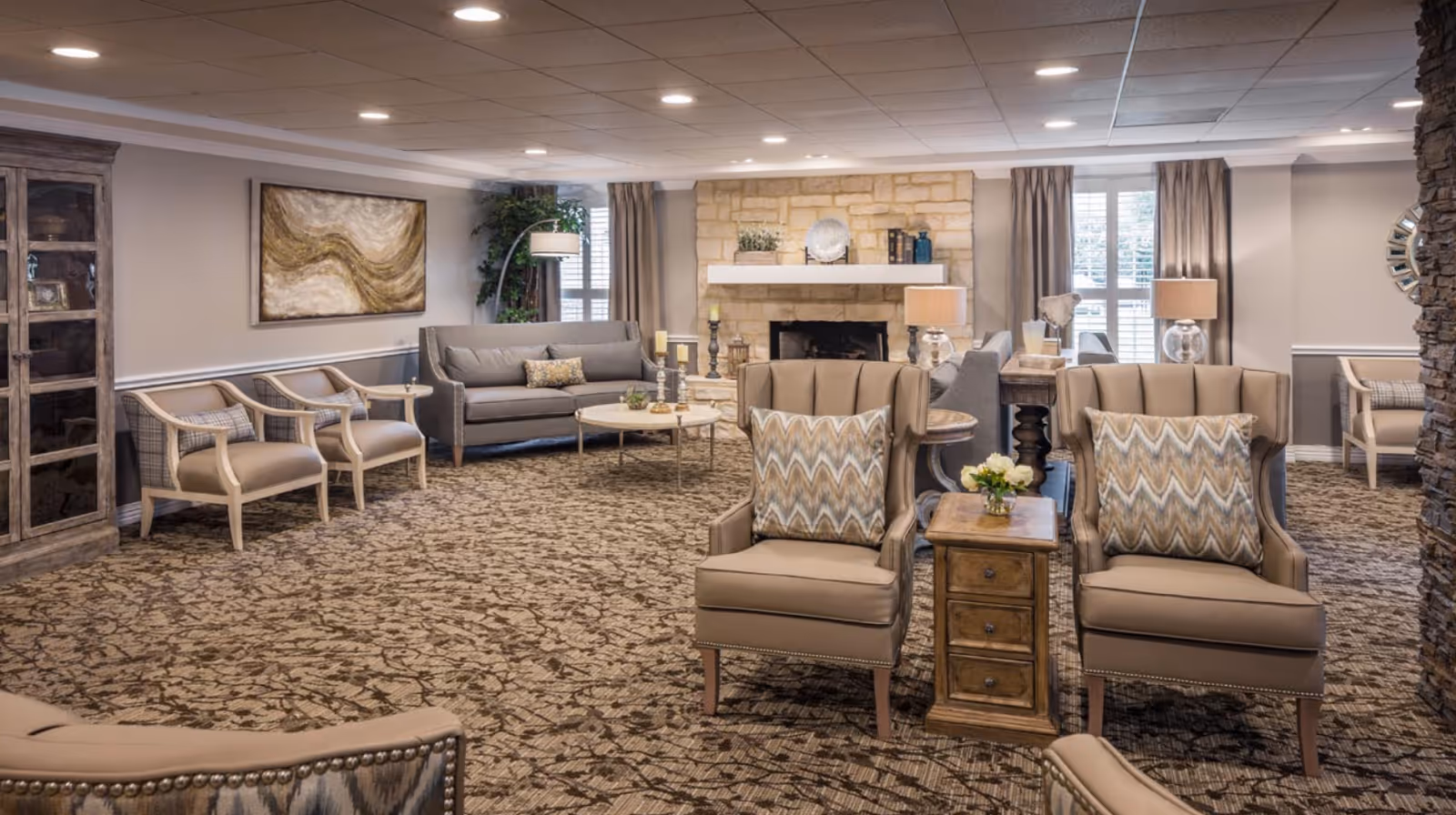 A cozy lobby area featuring comfortable seating, a stone fireplace, and decorative artwork. The space is well-lit with natural light and has a warm, inviting atmosphere.