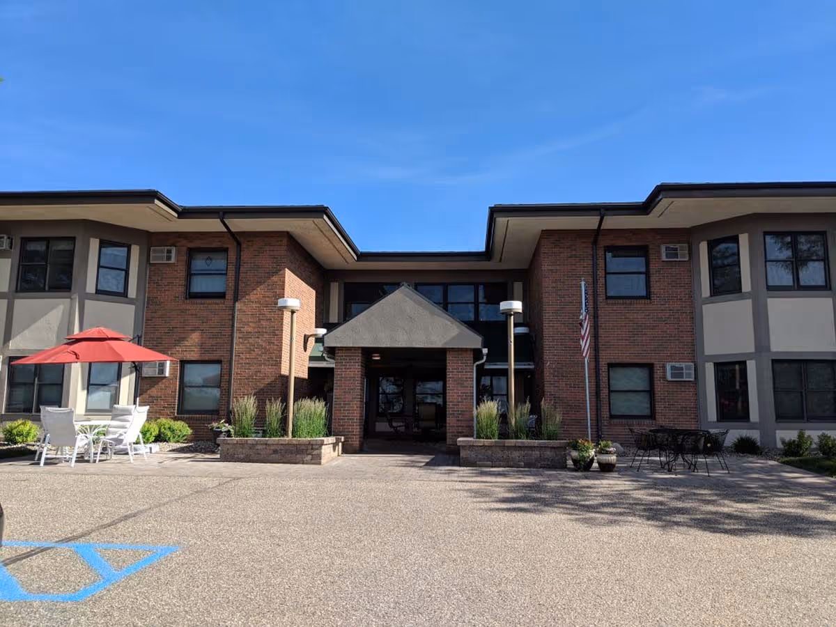 Two-story brick building front entrance with outdoor seating, a red umbrella, and an American flag under a blue sky.