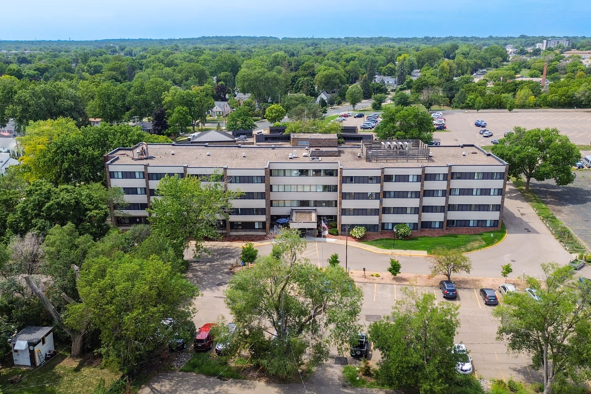 Aerial view of a multi-story health care center building surrounded by trees and parking lots, with a clear sky in the background.