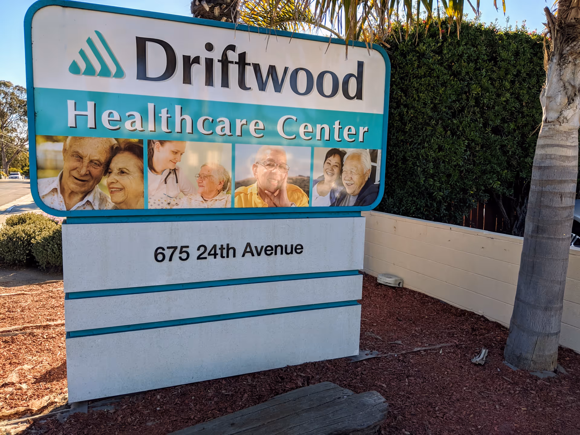 Outdoor sign for Driftwood Healthcare Center with photos of seniors and the address '675 24th Avenue'.