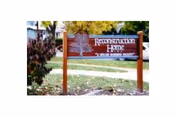 A wooden sign outdoors with the text 'Reconstruction Home' and a tree logo, surrounded by grass, bushes, and trees with autumn foliage.