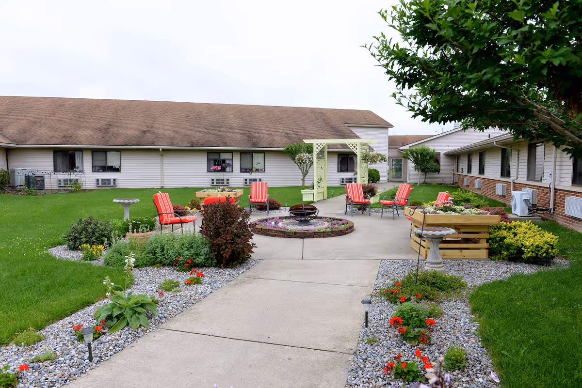 Courtyard with red chairs around a central firepit, planter boxes, a pergola, and a concrete path between single-story building wings.