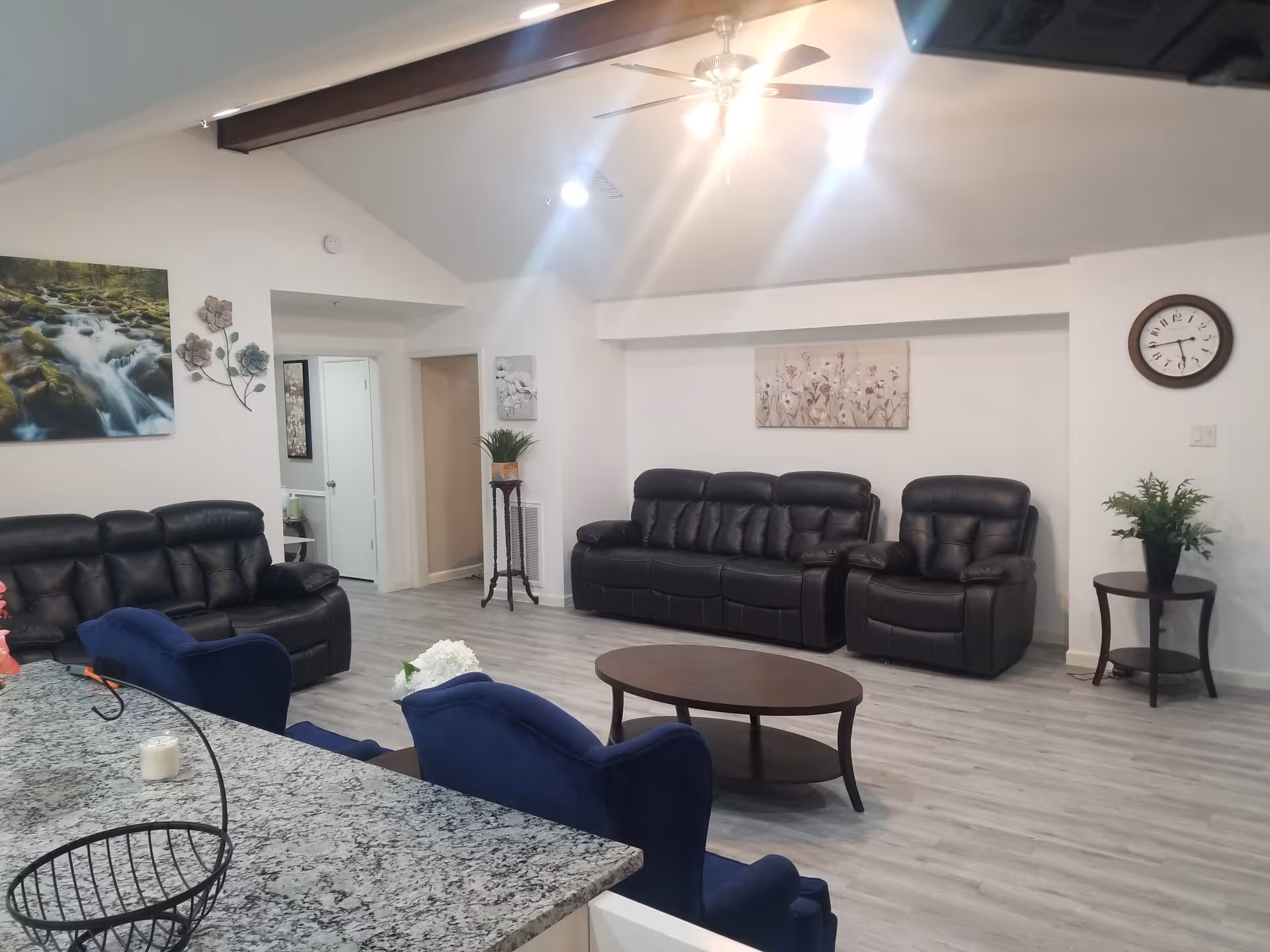Spacious living room with black leather sofas, blue armchairs, a coffee table, and a granite countertop in the foreground.