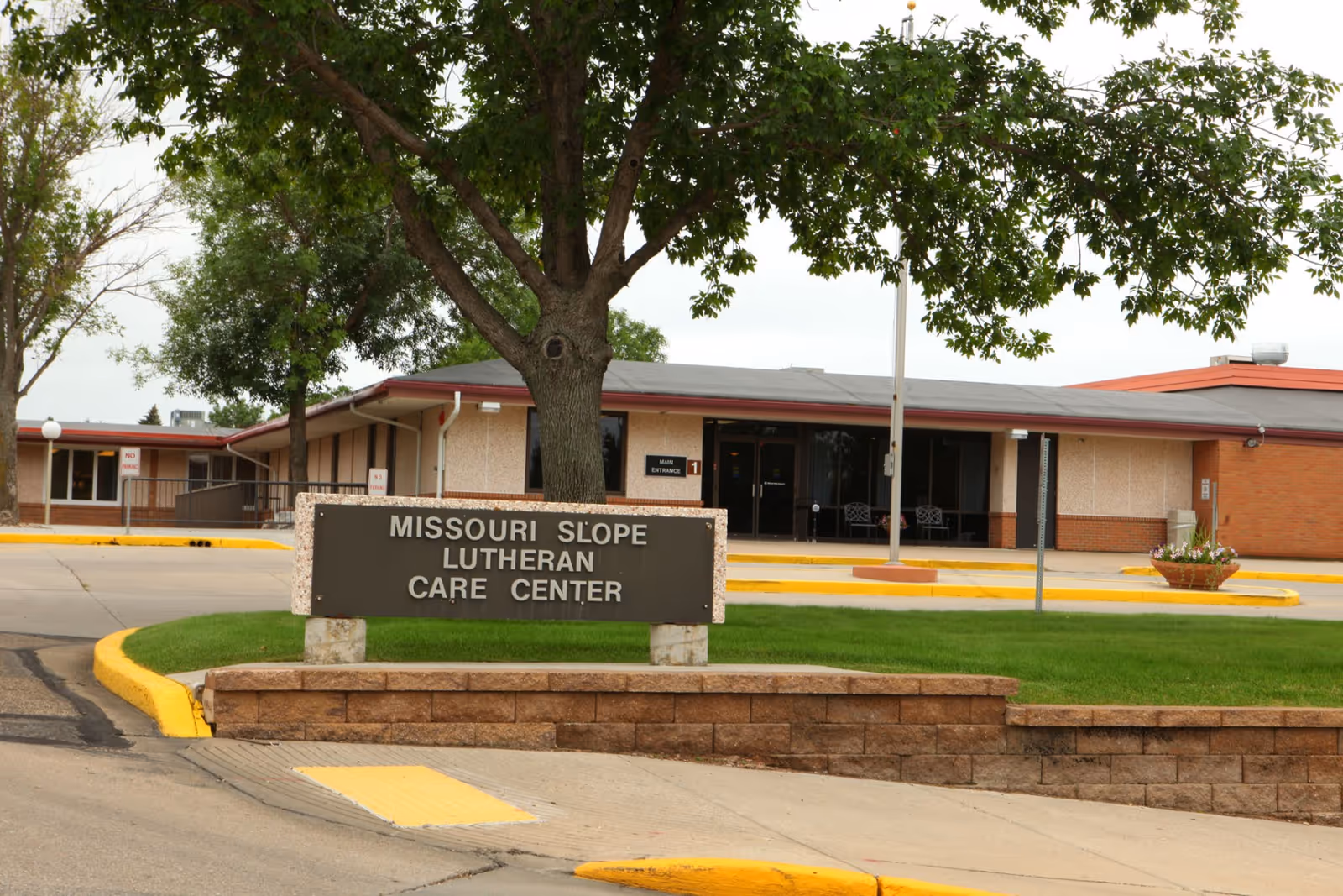 Sign reading 'Missouri Slope Lutheran Care Center' in front of a one-story care facility building with trees and a driveway.