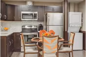 Small modern kitchen with a round dining table, stainless steel appliances, dark cabinets, and a stacked washer-dryer unit.