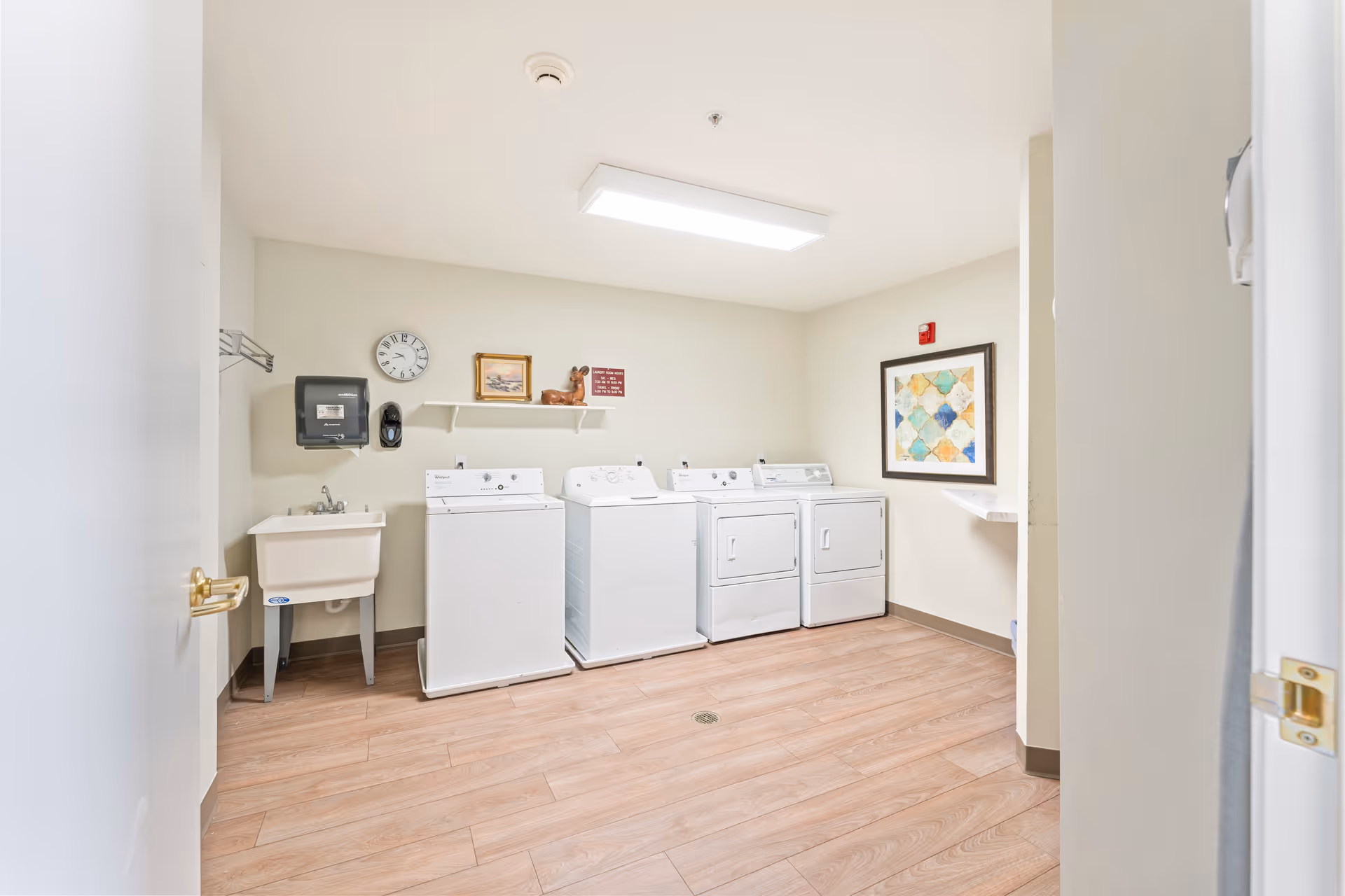 A clean laundry room with three washers, two dryers, a utility sink, and framed wall decor.