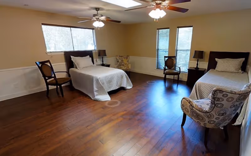 Spacious shared bedroom with two twin beds, hardwood floors, chairs, nightstands, windows, and ceiling fans.