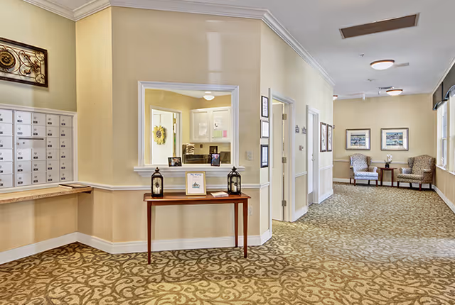 Well-lit reception hallway with mailboxes, a small table holding lanterns and a framed sign, and a seating area at the end of the corridor.