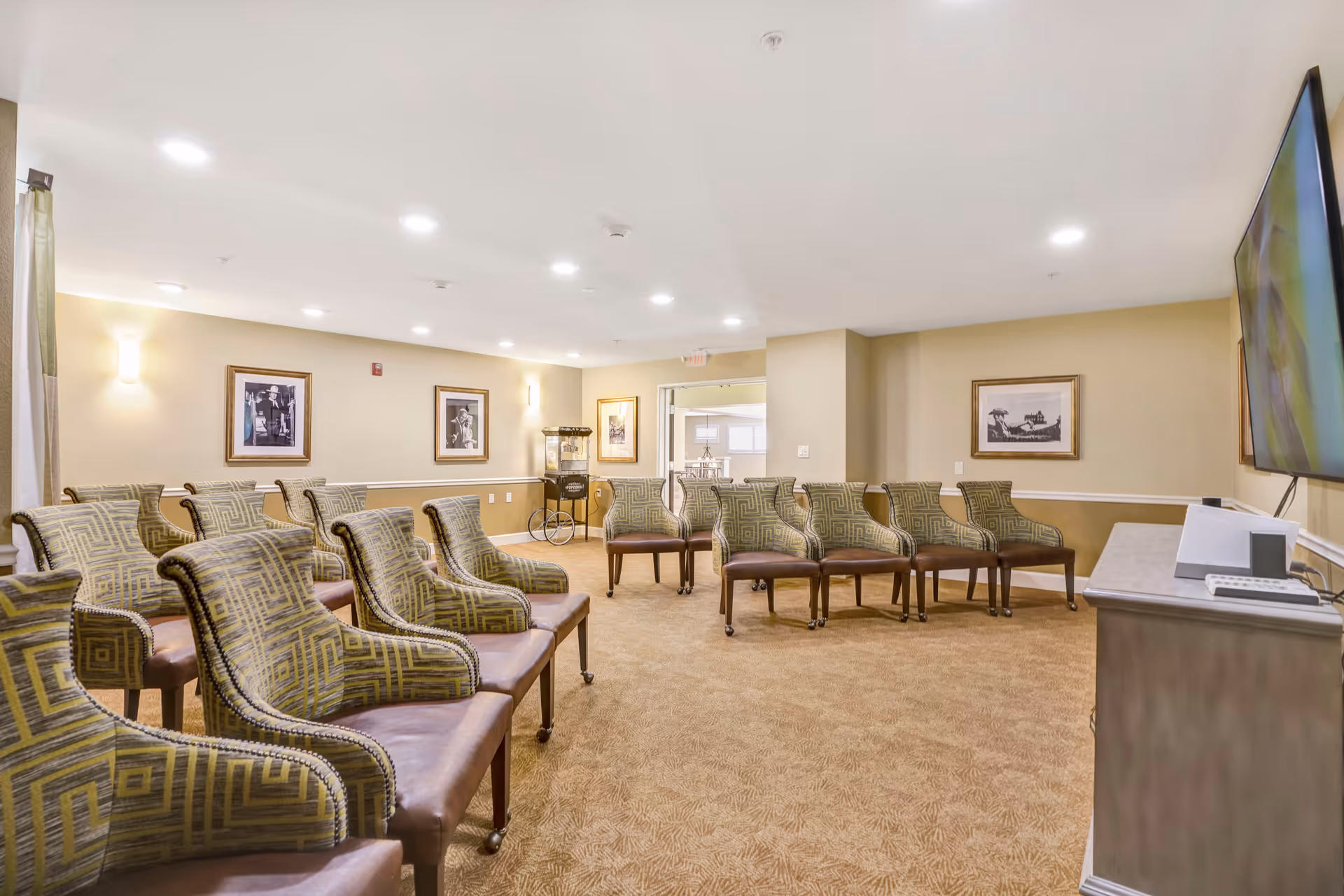 A spacious lounge with rows of patterned armchairs arranged facing a wall-mounted TV and framed artwork on the walls.