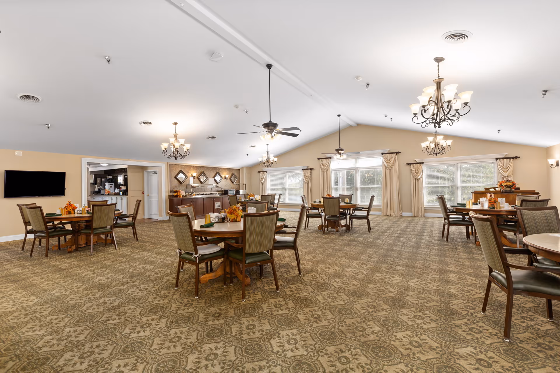 Spacious dining room with round tables and chairs, chandeliers, and large windows.