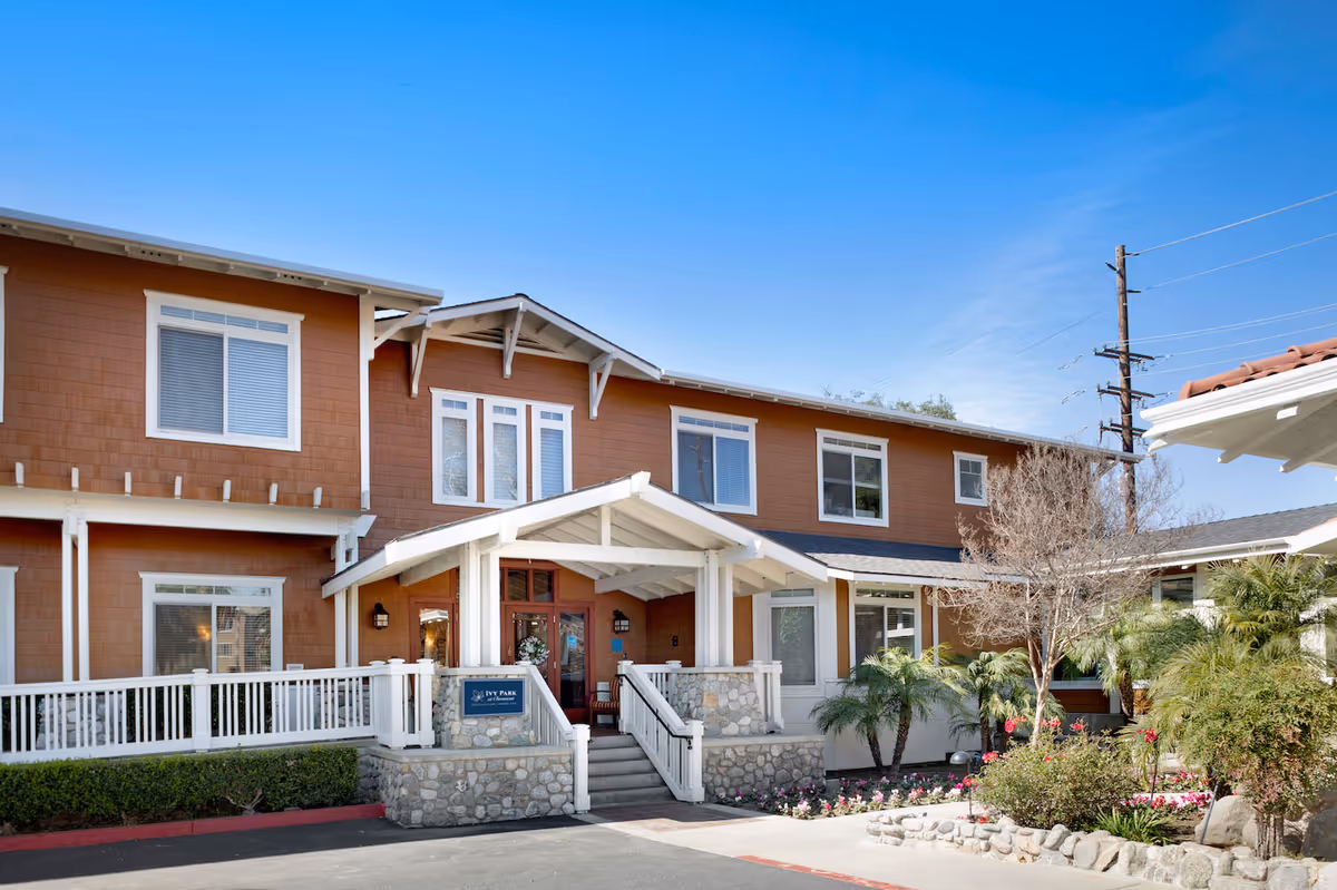 Front entrance of a two-story brown building with a covered porch, stone steps, and landscaped beds.