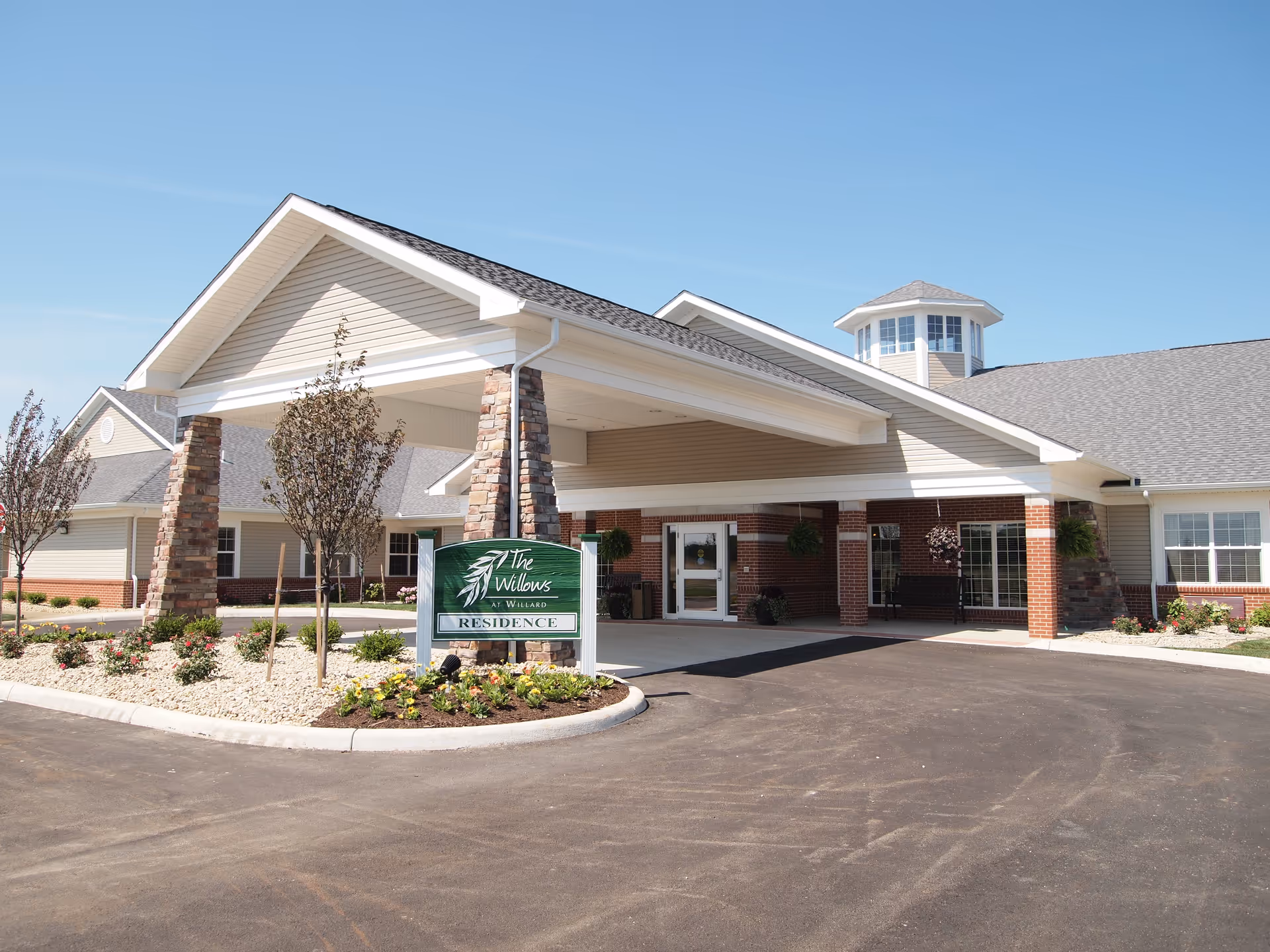 Front entrance of The Willows at Willard senior living residence featuring a covered porte-cochere, sign, and landscaped driveway.