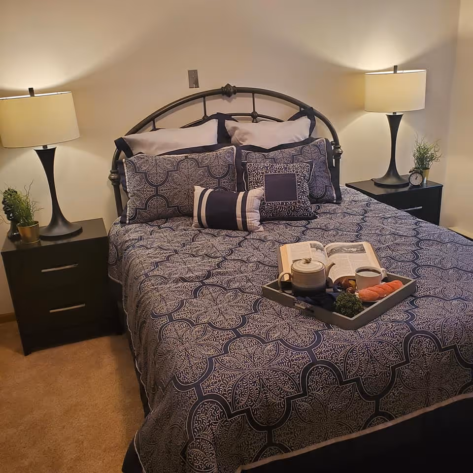 A neatly made bed with patterned blue bedding, decorative pillows, bedside tables with lamps, and a breakfast tray on the bed.