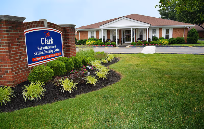 Front exterior of Clark Rehabilitation & Skilled Nursing Center showing a brick sign, landscaped lawn, and the building's entrance.