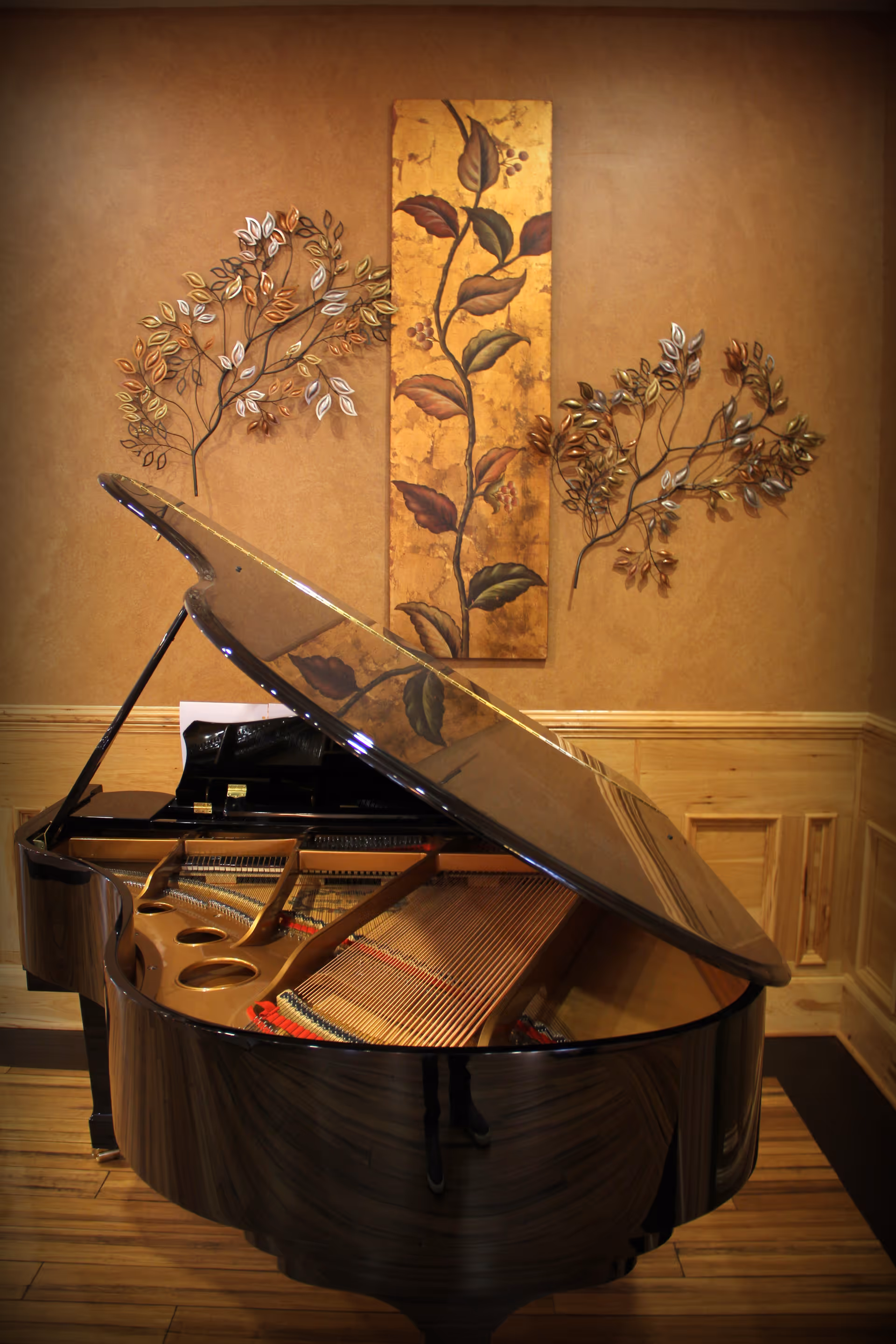 A grand piano with its lid open in a warmly decorated room beneath floral wall art.