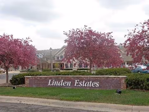 Linden Estates brick sign with pink blossoming trees and a building in background