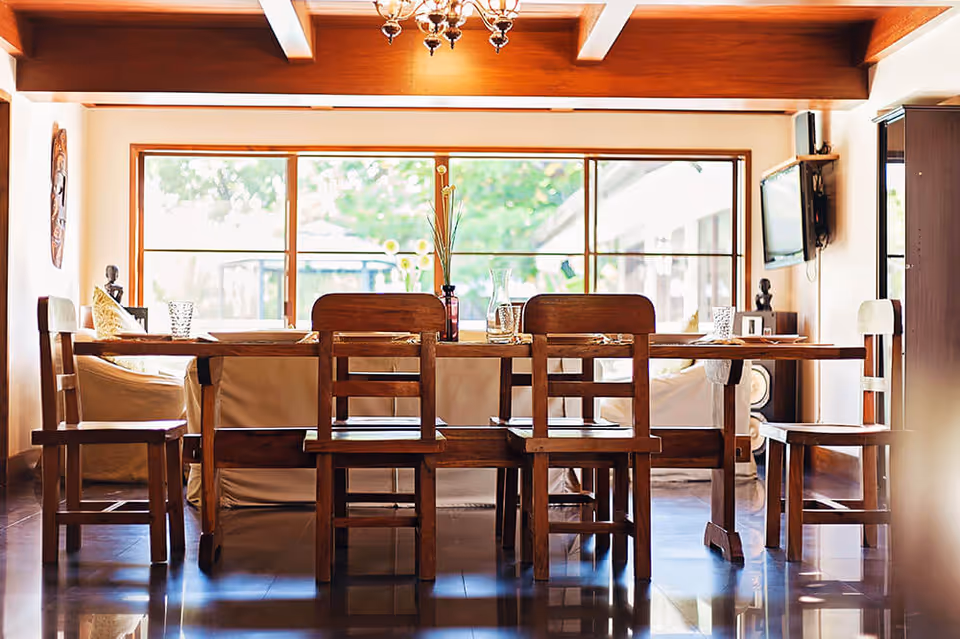 Sunlit dining room with a wooden table and chairs in front of a large window.