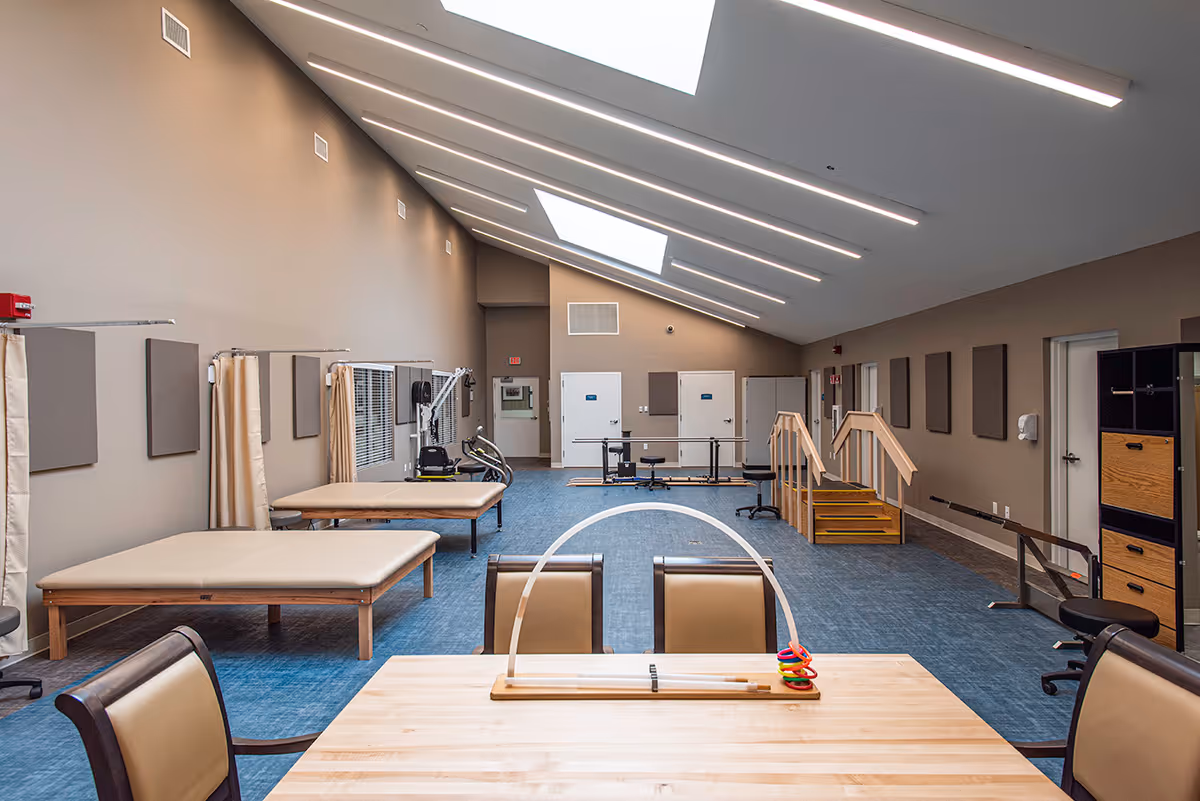 Spacious rehabilitation therapy room with treatment tables, exercise equipment, practice stairs, and skylights.
