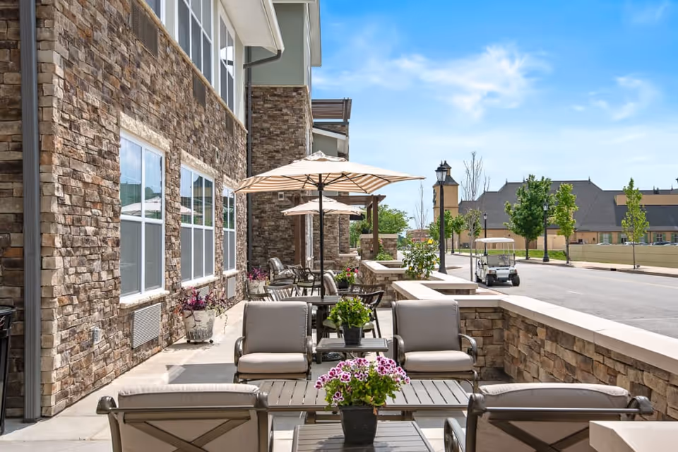 Outdoor patio with cushioned chairs, tables, umbrellas and a stone building facade.