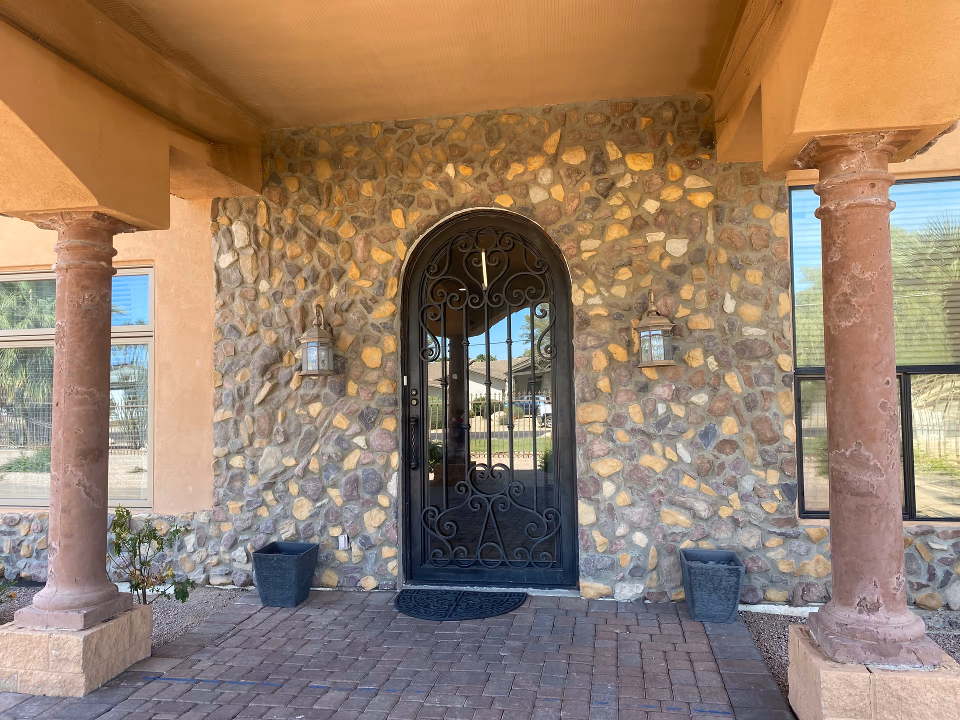 Stone-fronted building entrance with an arched wrought-iron door flanked by columns and wall lanterns.
