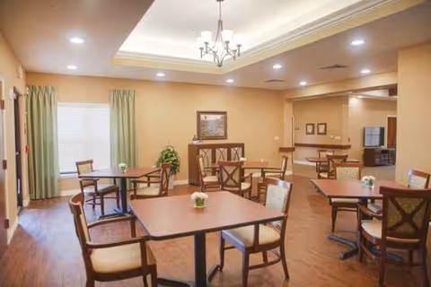 Bright dining room in a senior facility with multiple tables, chairs, and chandeliers.