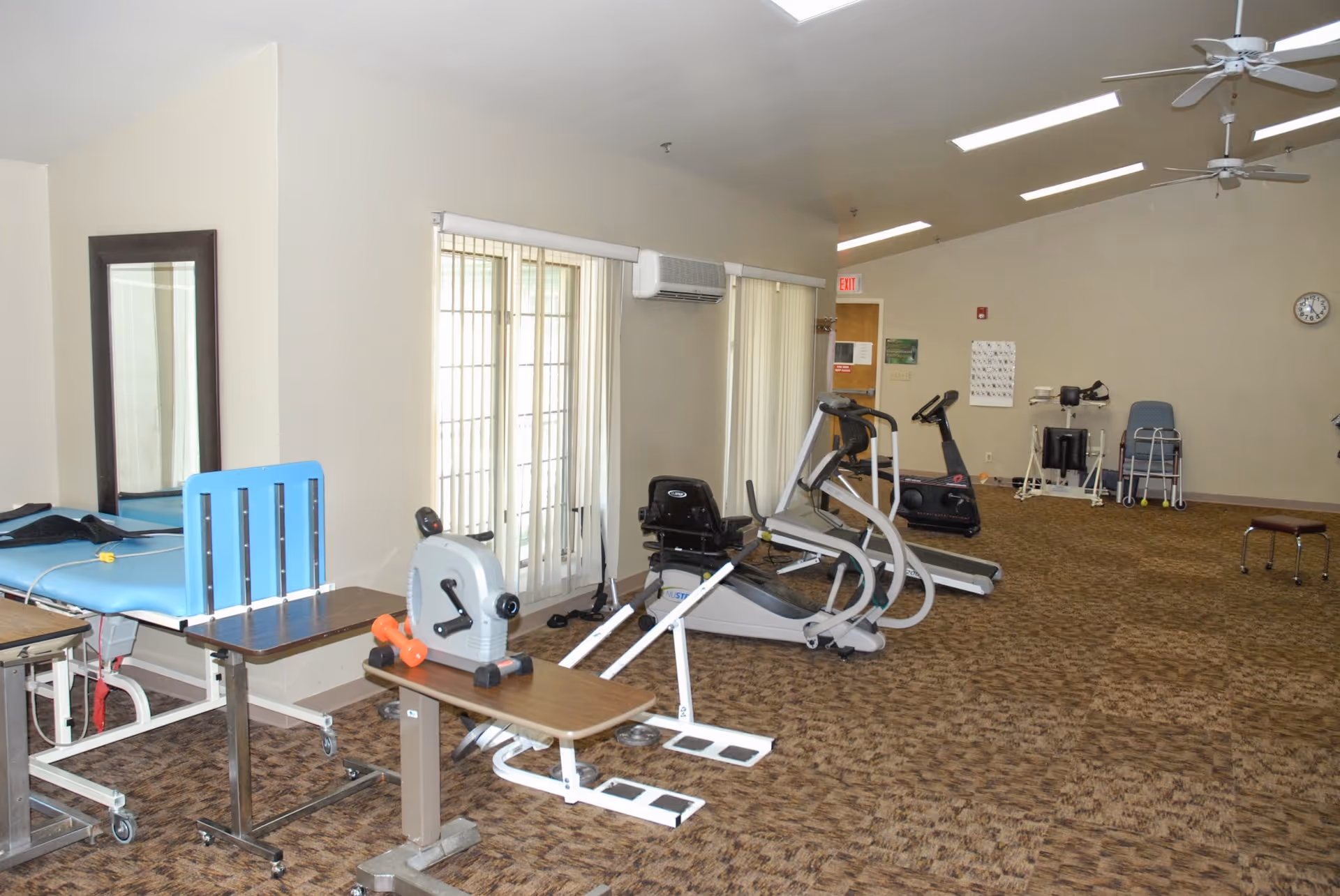 A spacious rehabilitation/exercise room with therapy tables, stationary bikes, treadmills and other fitness equipment.