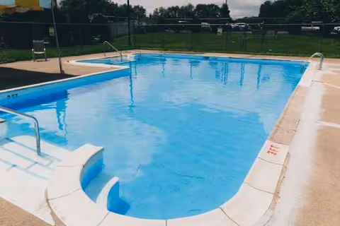 Outdoor pool at a senior facility with steps, railing, and a surrounding fence.