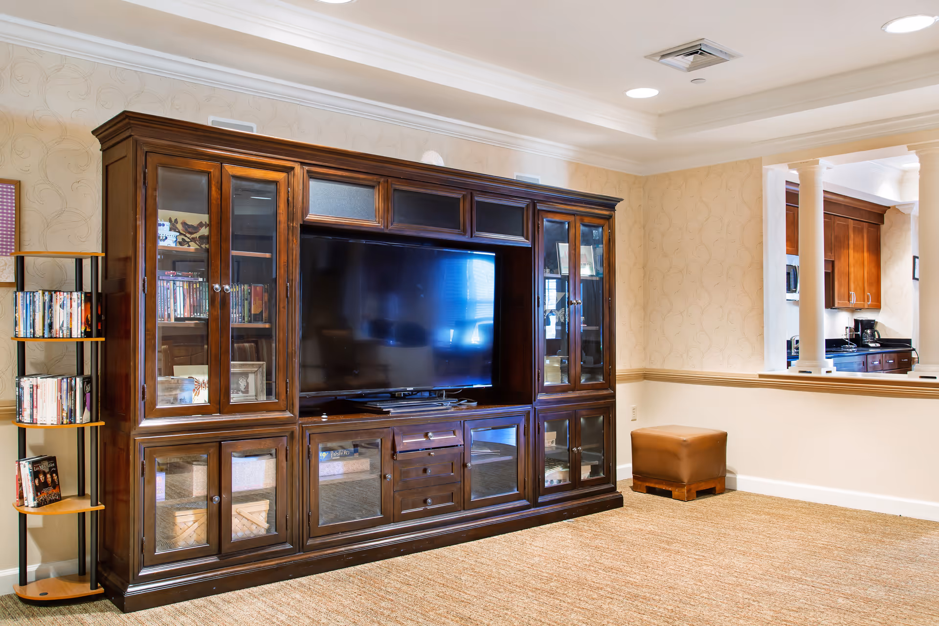 Spacious living room with a large dark wooden entertainment center housing a flat-screen TV, a DVD rack, and an open pass-through to the kitchen.