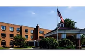 Brick multi-story healthcare building with a covered entrance, American flag on a flagpole, and surrounding landscaping.