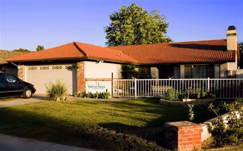 Front exterior of Betty's Homes with a red-tiled roof and a fenced yard.