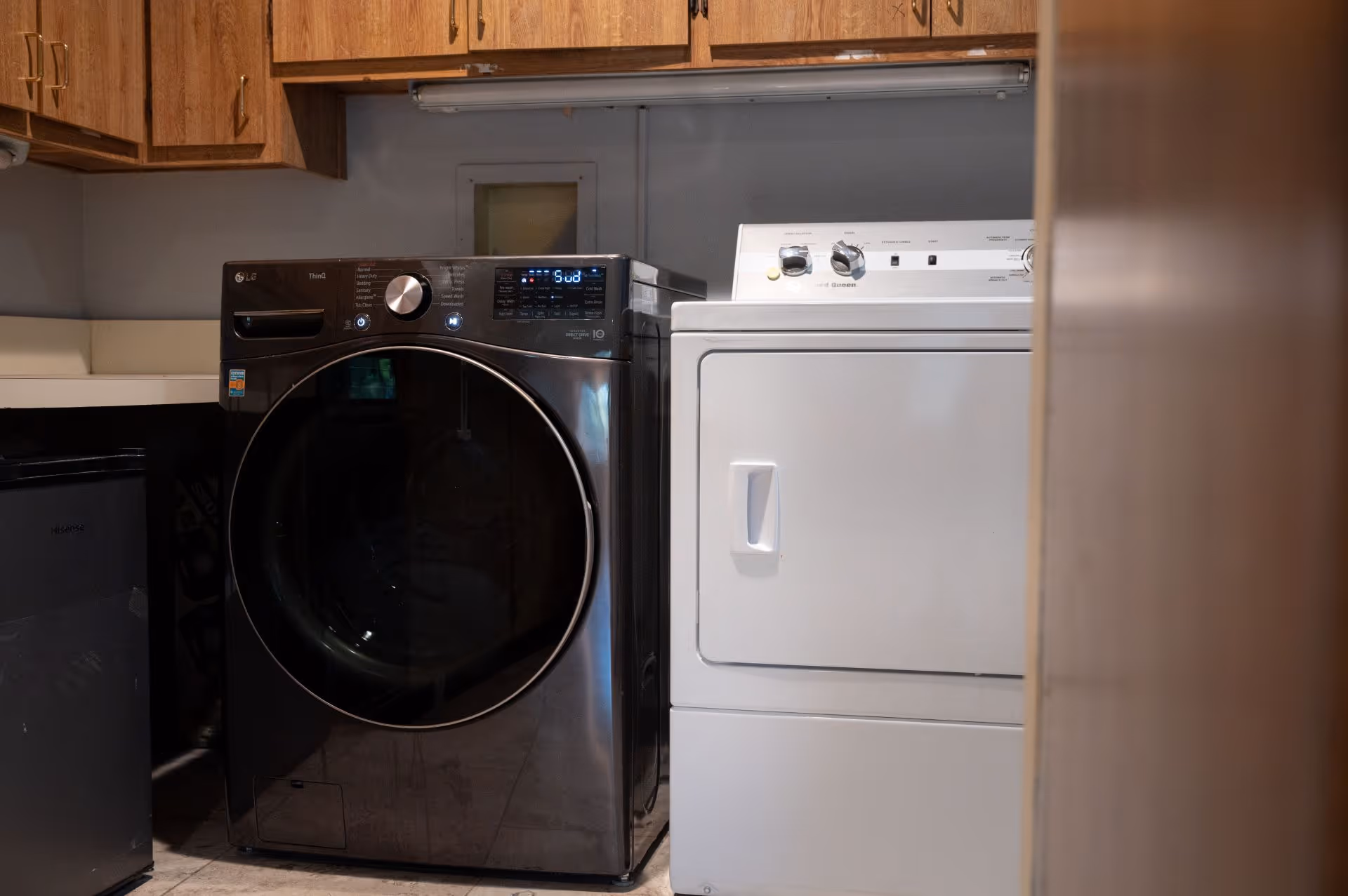 A laundry area with a front-loading black washing machine and a white dryer beneath wooden cabinets.