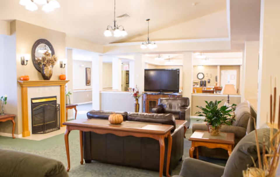 Common area living room with sofas, a fireplace, a TV, and tables in a senior living facility.