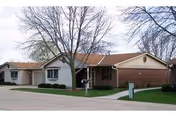 Single-story residential building with a brick and siding exterior, a large leafless tree in front, and a well-maintained lawn and sidewalk leading to the entrance.