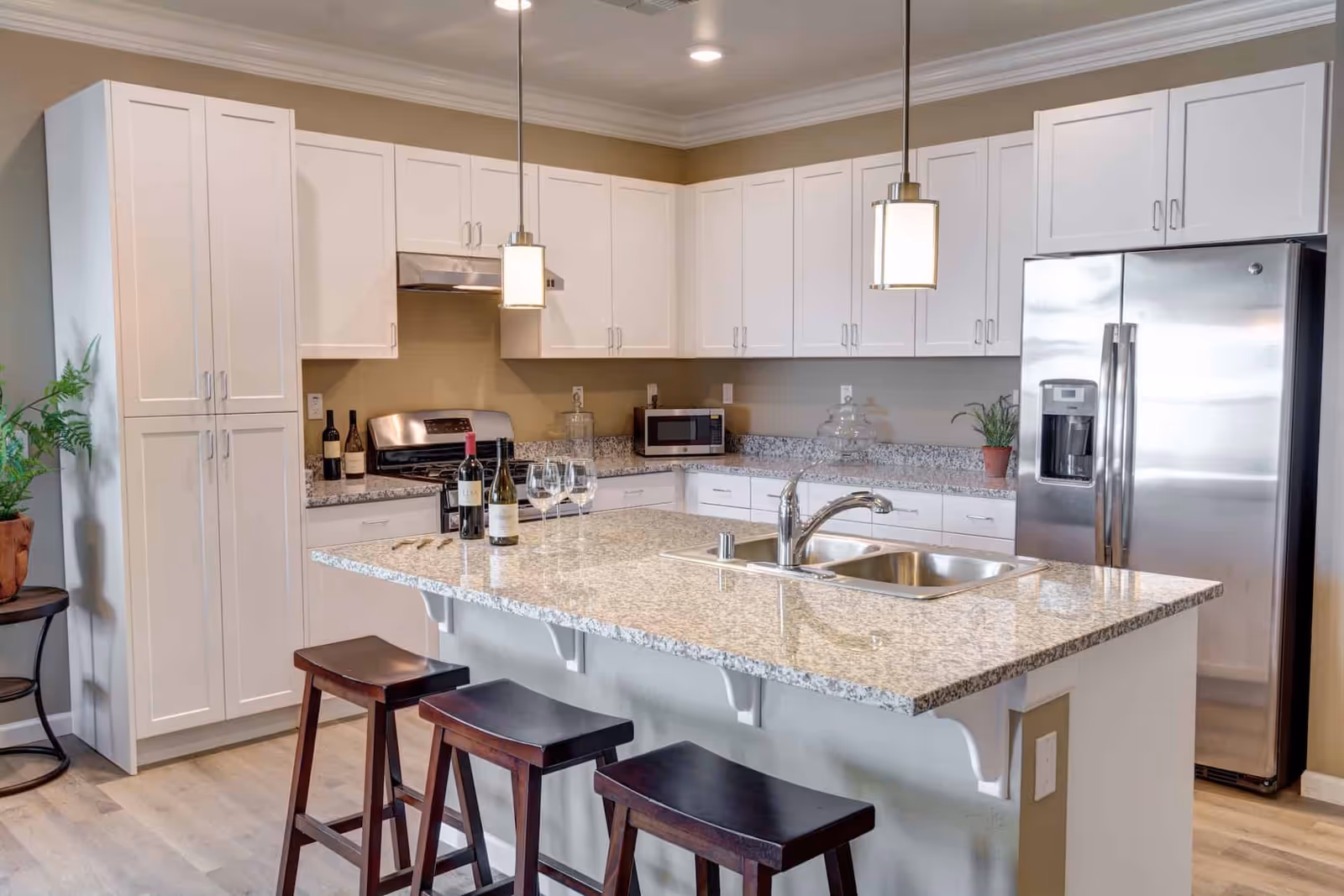 Modern kitchen with a large granite island, stainless steel appliances, white cabinets, and three bar stools.
