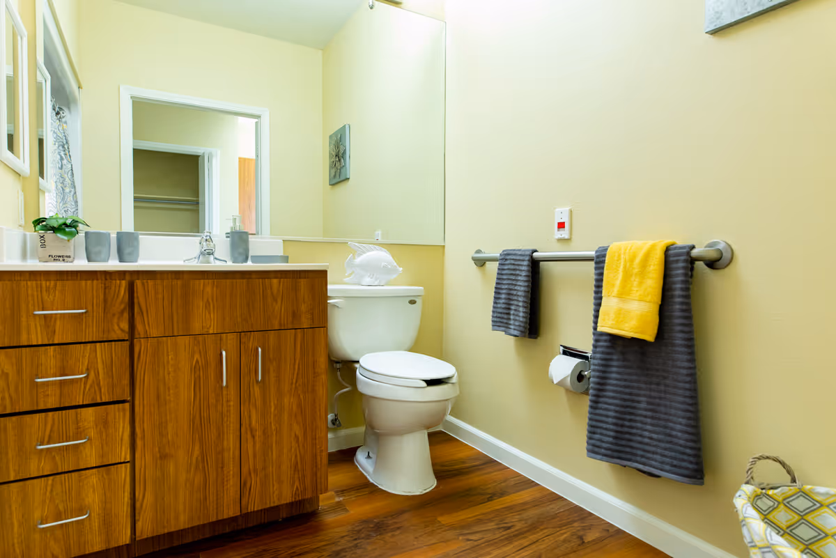 Bathroom featuring a wooden vanity with sink and mirror, a toilet, and towels hanging on a wall-mounted bar.